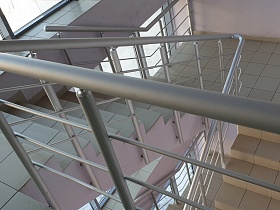 квадратная плитка на ступенях лестницы с металлическими перилами прозрачного современного подъезда