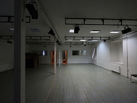 софиты на белом потолке просторного танцевального балетного зала с белыми стенами и белым дощатым полом в подземелье со сводами
