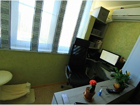 зеленый шкаф с полочками , монитор с клавиатурой на полукруглом компютерном столе на открытой лоджии современной  двухкомнатной квартиры новосторя