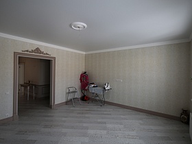 гладильная доска, напольная вешалка с одеждой,лестница-стремянка в одном углу и напольная ваза в другом светлой гостиной загородного дома