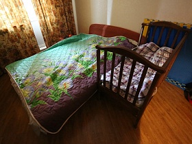 детский манеж у большой кровати с цветным стеганным покрывалом в спальне обычной квартиры в новостройке