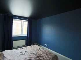 синие шторы на большом окне, синие стены и черный потолок в  спальной комнате современной молодежной двухкомнатной квартиры