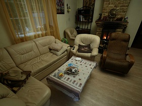 светлая мягкая мебель, журнальный столик со скатертью, этажерка с книгами у камина в гостиной зонированной комнаты семейного даухэтажного дома в глухом лесу