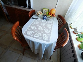 ваза с фруктами, салфетки, солонки и сахарница на обеденном столе с белой скатертью в кухне большой квартиры врача