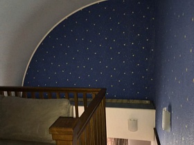 фрагмент звездного неба на стене над лестницей,ведущей на второй этаж с белым диваном у деревянных перил