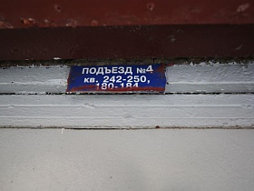 синяя вывеска с номерами квартир над входной серой металлической дверью в подъезд дома эпохи СССР