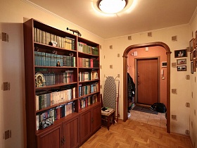большой книжный шкаф ,стул и гладильная доска у арочного дверного проема в песочном холле трешки