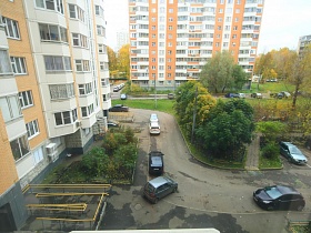 вид из окна квартиры на придомовую территорию с проезжей дорогой, полисадником и зеленым участком в жилом квартале