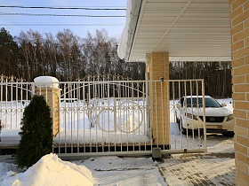 белая машина у открытых ворот белого металлического забора на въезде в гараж под навесом