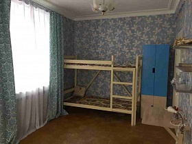 настольная лампа в стиле хай-тек над бежевой поверхностью складного столика под полками на голубой стене спальной комнаты с деревянной двухярусной кроватью и шкафом для одежды