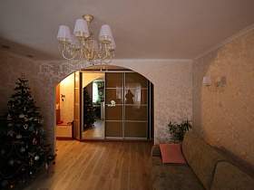 бежевый мягкий диван у стены светлой гостиной с люстрой и бра с белыми плафонами