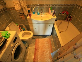 полотенца на стиральной машинке, санузел, белая раковина на шкафчике, белая ванна, зашитая зеленой плиткой в ванной комнате с двухцветной плиткой на стенах евро квартиры с видом на Москву и парк