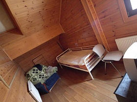 в мансарде под деревянным потолком уютно разместились кровать, синее кресло и телевизор на тумбе