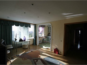 стол у большого окна с зелеными шторами,светлые стулья и ковер с арнаментом на полу светлой гостиной евро квартиры с видом на Москву и парк