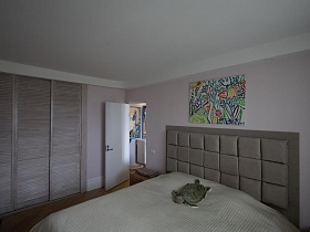 мягкая черепаха на светлом покрывале большой кровати, встроенный шкаф-купе в спальной комнате красивой стильной трехкомнатной квартиры