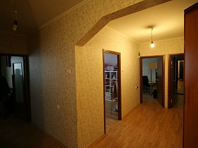 арочный дверной проем объединяющий прихожую и длинный коридор с одинаковыми обоями на стенах большой трехкомнатной квартиры в переезде