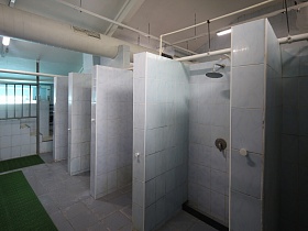 просторная светлая комната в лофт здании с индивидуальными белыми душевыми кабинками, зеленой дорожкой на кафельном полу и ступенями, ведущими наверх к бассейну для съемок кино