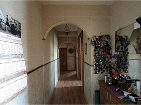 трюмо и коллекция солнцезащитных очков на светлой стене прихожей у арочного дверного проема простой сталинской квартиры