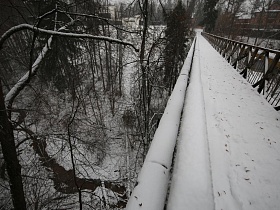 длинные трубы под высоким металлическим подвесным пешеходным мостом над речкой в низине