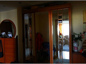 высокий шкаф-купе с зеркальными дверцами и цветы в вазе на шкафчике в коридоре трехкомнатной квартиры панельного дома