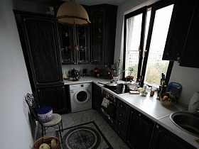 темнокоричневая кухня с высокими шкафами в простой трехкомнатной семейной разрисованной квартире