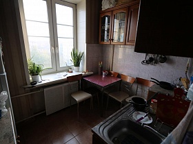 небольшой квадратный столик со стульями в углу кухни у окна с комнатными цветами на подоконнике квартиры сталинки