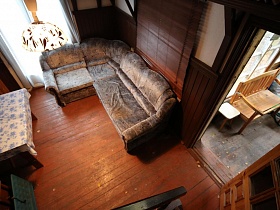 общий вид гостиной комнаты с угловым диваном с высоты деревянной лестницы в небольшом домике среди новостроек