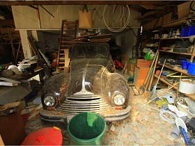 ретро машина в гараже с многочисленными хозяйственными предметами на полу и на полках стеллажа