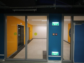 двери лифта в ярких желтых стенах просторного холла через стеклянные раздвижные двери подземного паркинга