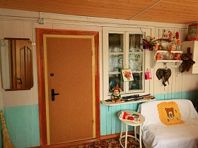 деревянный навесной шкаф и белая полочка с мягкими и резиновыми игрушками у окна двери в комнаты деревянной избы в деревне