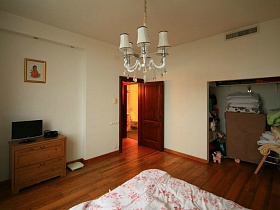 телевизор на деревянном коричневом комоде у стены с картиной, открытая ниша в стене спальной комнаты с белыми стенами евро квартиры в кирпичном доме