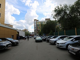 припаркованные автомобили на широкой асфальтированной дороге вдоль зеленного металлического забора и у стен здания "Казино"