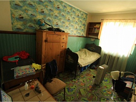 большой стол, стул, глобус на деревянном шкафу, обогреватель на полу, кровать и деревянная открытая полка у окна с белой гардиной в детской для съемок кино