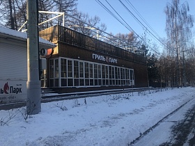 кафе-стекляшка с белой вывеской на фасаде деревянного здания с открытой террасой на крыше вдоль проезжей автомобильной дороги в зимнее время