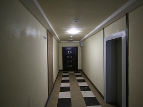 длинный светлый коридор на этаже с шахматным полом к входным дверям квартиры современного многоэтажного дома