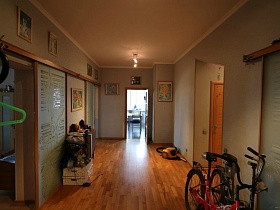 красный и черный велосипеды, желтый пылесос,короб с игрушками у складного стола в светлой прихожей с открытой дверью на кухню трехкомнатной квартиры