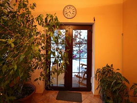 круглые часы на стене и коврик у входной двери просторной комнаты уютной лесной дачи в соснах