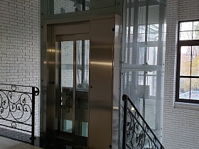 серая и черная плитка на полу лестничной площадки с черными фигурным перилами у стеклянных дверей стильного лифта современного жилого дома