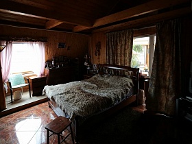 резная спинка деревянной кровати с меховым покрывалом у окна с коричневыми шторами в спальной комнате семейной классической дачи
