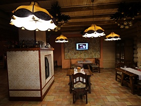 белые салфетки на поверхности деревянных сервированных столов в зале с телевизором на стене, высоким шкафом у стены и русской печью в красивом ресторане в стиле сруба
