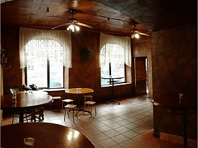 барные столики и обычные круглые с табуретками вокруг на полу с квадратной плиткой в уютном зале со светлыми короткими гардинами на окнах и люстрами-вентиляторами на потолке классического рюмочной, бутербродной, закусочной СССР