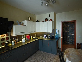 белые верхние и темные нижние шкафы двухцветной мебельной стенки светлой кухни с черными стульями вокруг обеденного стола со скатертью