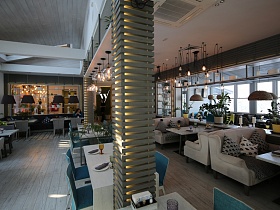 подсвеченные колонны под декоративной деревянной решеткой между белыми столиками с голубыми стульями по центру просторного зала стильного ресторана