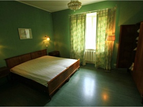коричневая деревянная кровать с белым матрасом, прикроватные тумбочки, шкаф для одежды в спальной комнате с зелеными стенами и шторами на окне второго этажа современного дома