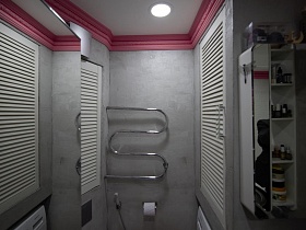 туалетные принадлежности на полках белого шкафа с зеркальной дверцей, полотенцесушитель над санузлом у светлых стен ванной комнаты трехкомнатной квартиры