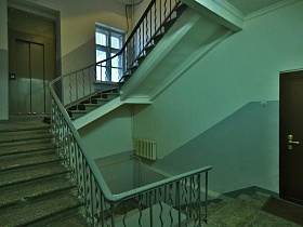 чистый светлый подъезд с серыми панелями стен, окнами на площадках винтовой лестницы, ковриками у входных дверей жилых квартир на этажах дома эпохи СССР