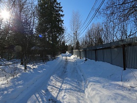 расчищенная от снега проселочная дорога вдоль забора загородного дома с камином