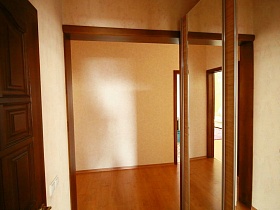 отражение коричневой деревянной двери хоз комнаты в зеркальных дверцах шкафа-купе в современной трехкомнатной квартире жилого дома