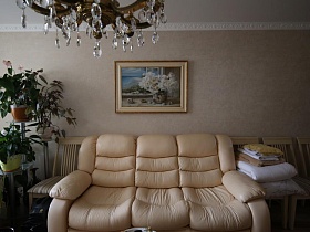 картина с цветами в рамке молочного цвета над мягким трехместным диваном в гостиной современной квартиры врача