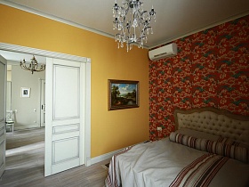 длинный круглый полосатый валик на белом покрывале с полосками деревянной кровати у яркой цветной красной стены спальной комнаты девчачьей дизайнерской квартиры